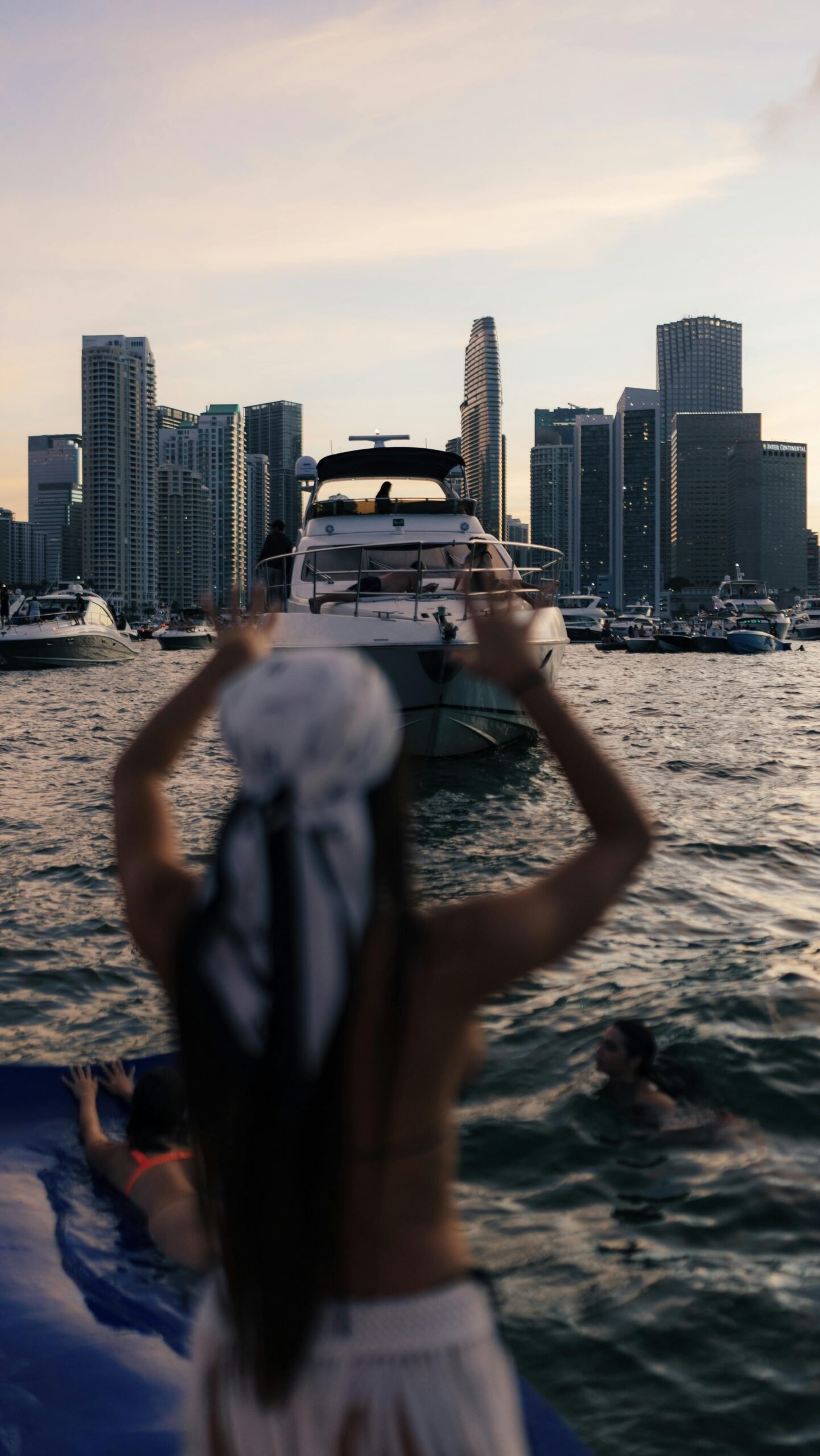 Luxurious yacht anchored near a city skyline at sunset, people enjoying the water.